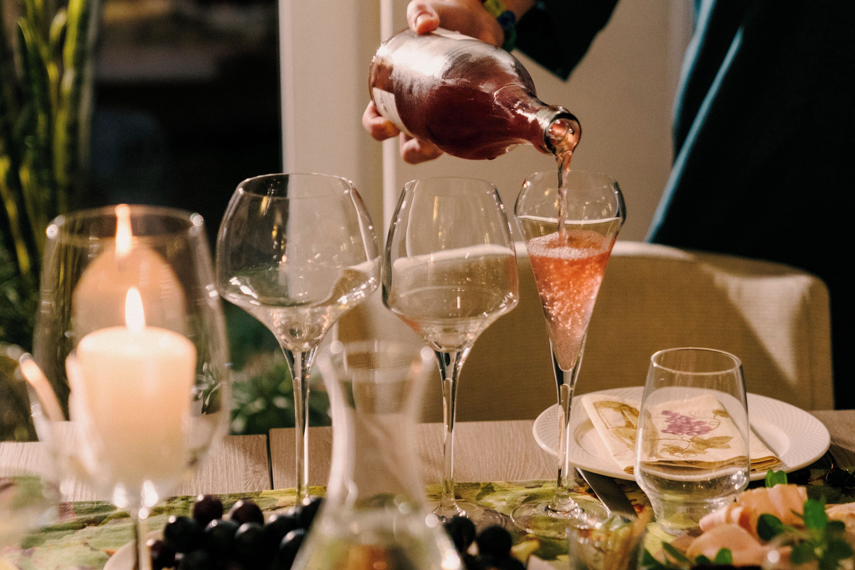 Una mesa servida con copas de vino, una vela y una botella siendo vertida.