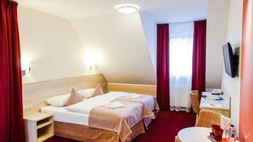 A hotel room with two beds, a desk, a chair, a TV, and a small table with a tray.