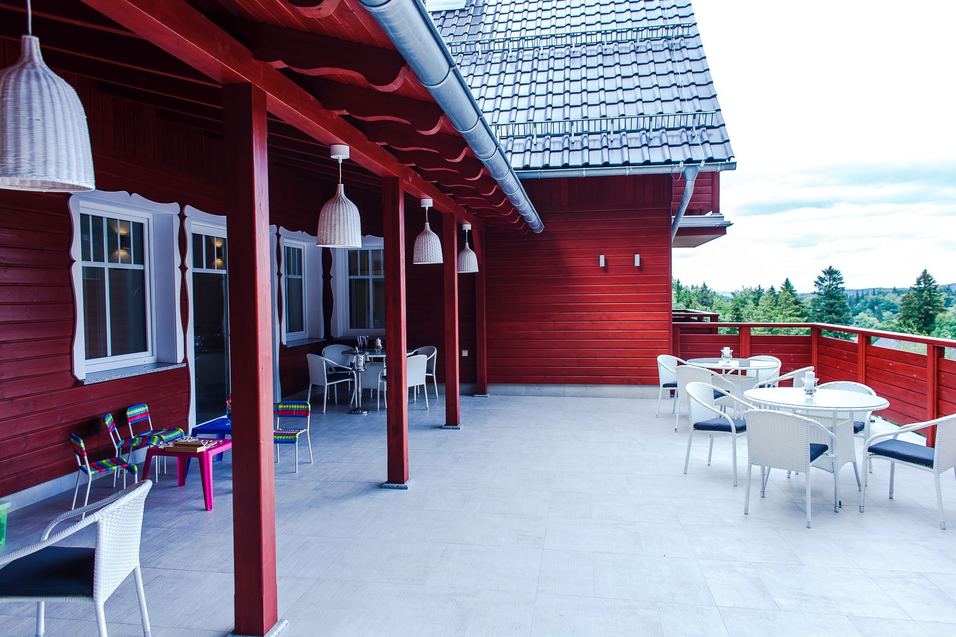 Un bâtiment en bois rouge doté d’un patio couvert, agrémenté de meubles en osier blanc et de lampes suspendues.