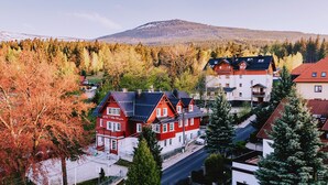 Um hotel vermelho e branco com montanhas ao fundo, rodeado por árvores de outono e outros edifícios.