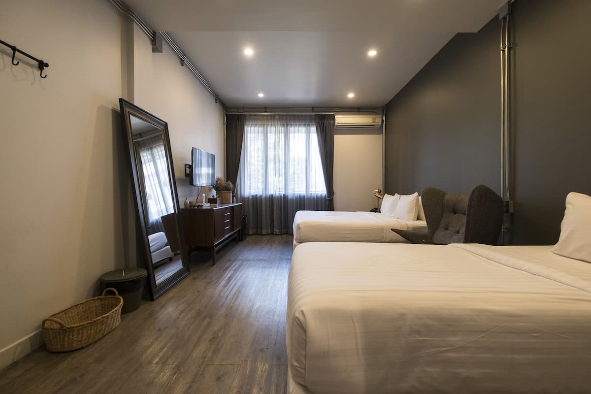 A hotel room with two beds, a desk, a chair, a mirror, a dresser, and a window with curtains.