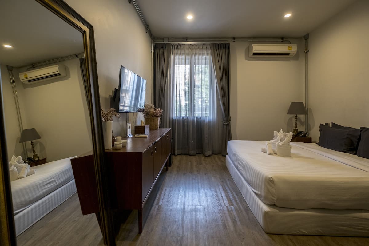 A hotel room with a bed, a dresser, a television, and an air conditioning unit.