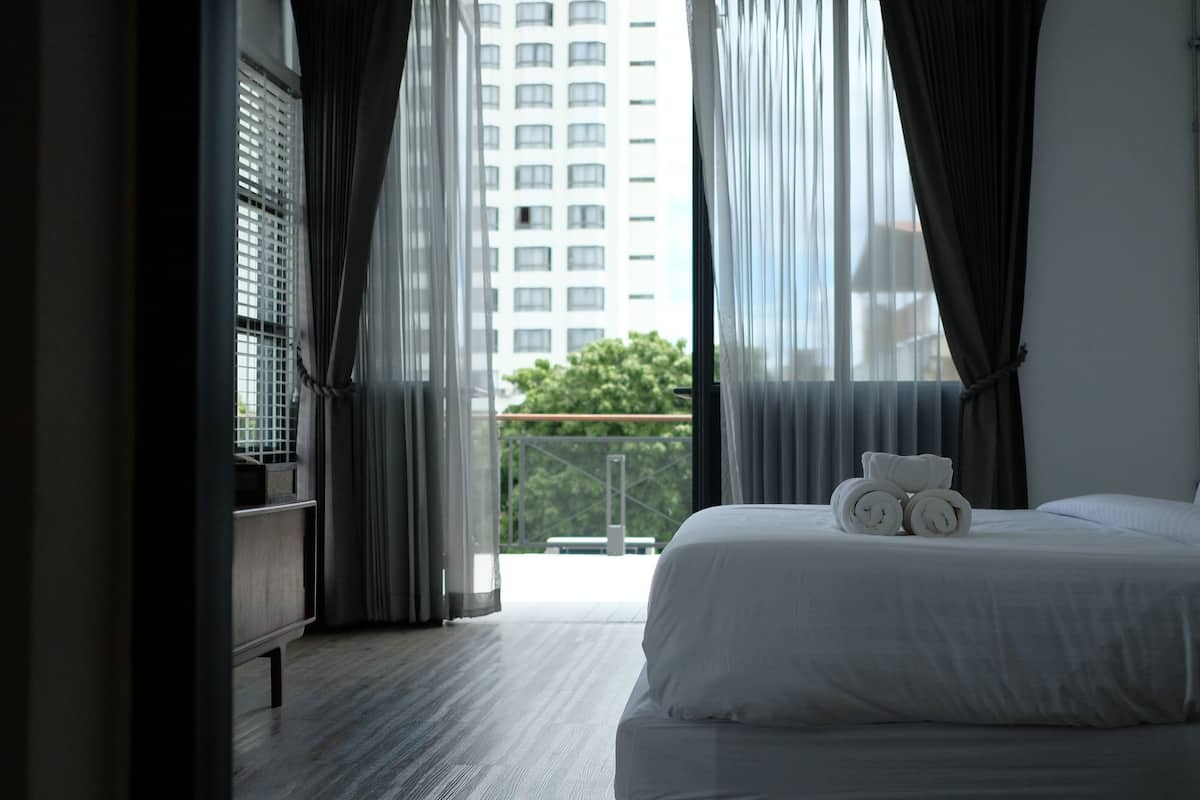 A hotel room with a bed, curtains, and a view of a building and trees.