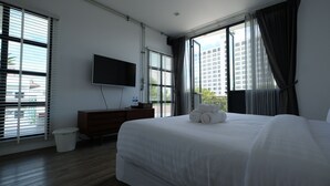 A hotel room with a large bed, a flat-screen TV mounted on the wall, a wooden dresser, and a window with blinds. - Iron32 Hotel (Chiang Mai)