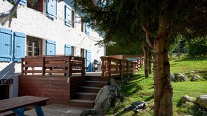 A wooden deck with picnic tables and a staircase leading to a building with blue shutters. - Chamonix Lodge (Chamonix-Mont-Blanc)