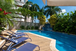 Una piscina al aire libre, sombrillas, sillones reclinables de piscina