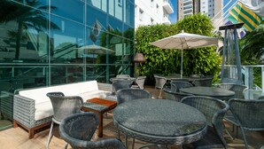 An outdoor seating area with wicker furniture, a white sofa, and a glass wall reflecting the surroundings. - Radisson Hotel Anapolis (Anapolis)