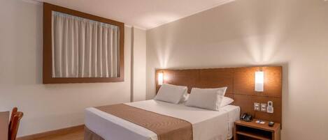 Una habitación de hotel con cama, mesita de noche y ventana con cortinas.