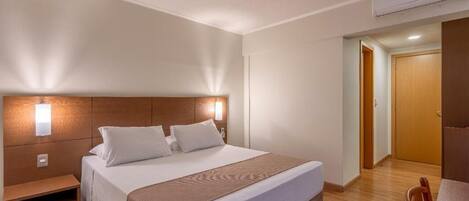 Una habitación de hotel con una cama grande, mesita de noche y cabecero de madera.