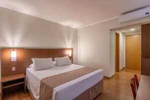 Una habitación de hotel con una cama grande, mesita de noche y cabecero de madera.