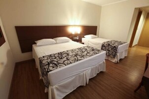 Habitación de hotel con dos camas, cabecera de madera y mesita de noche con lámpara.