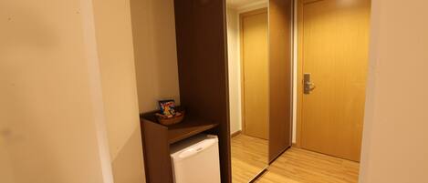 Una habitación compacta con piso de madera, un refrigerador blanco pequeño y una puerta de madera.