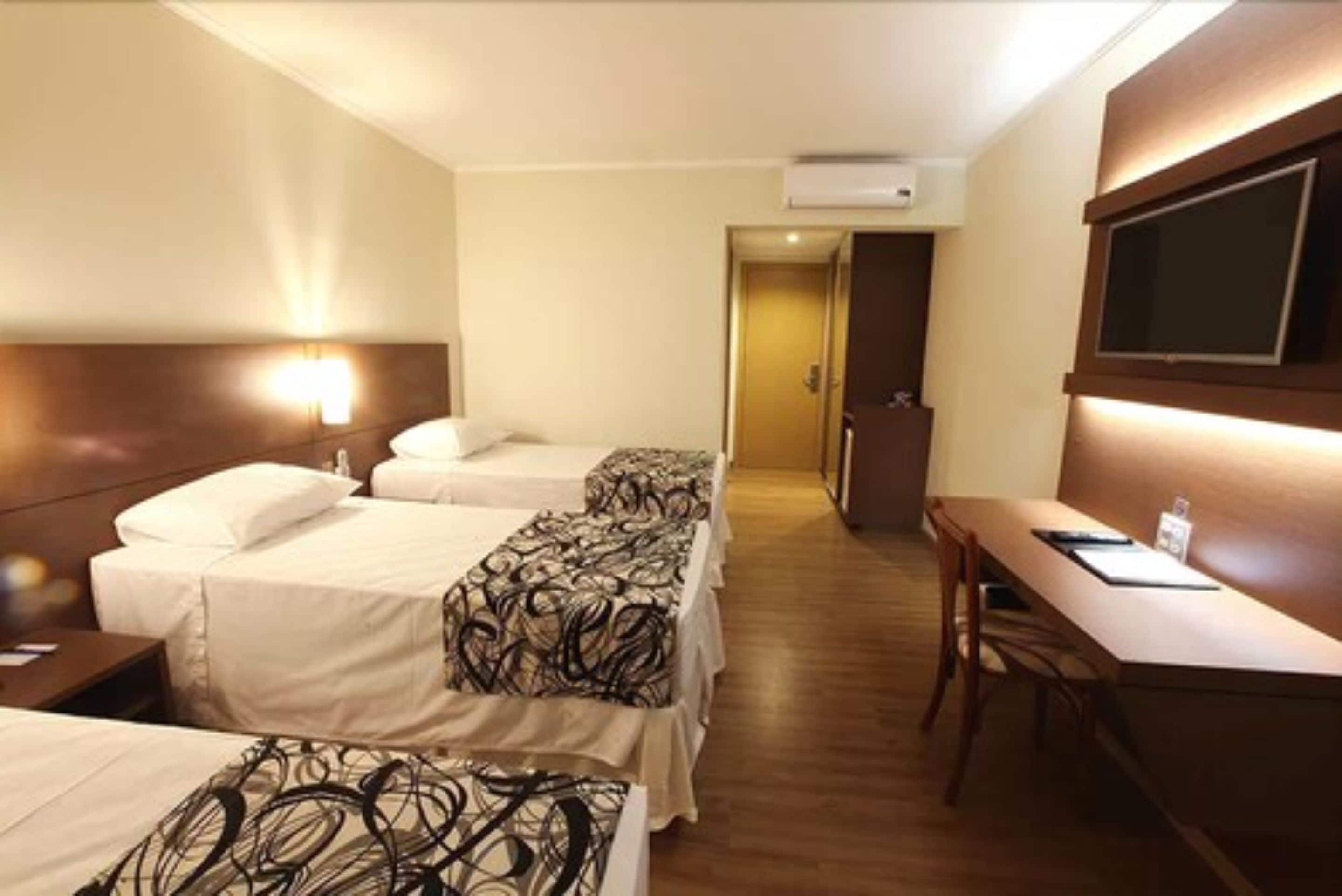 A hotel room with two beds, a desk, and a TV.