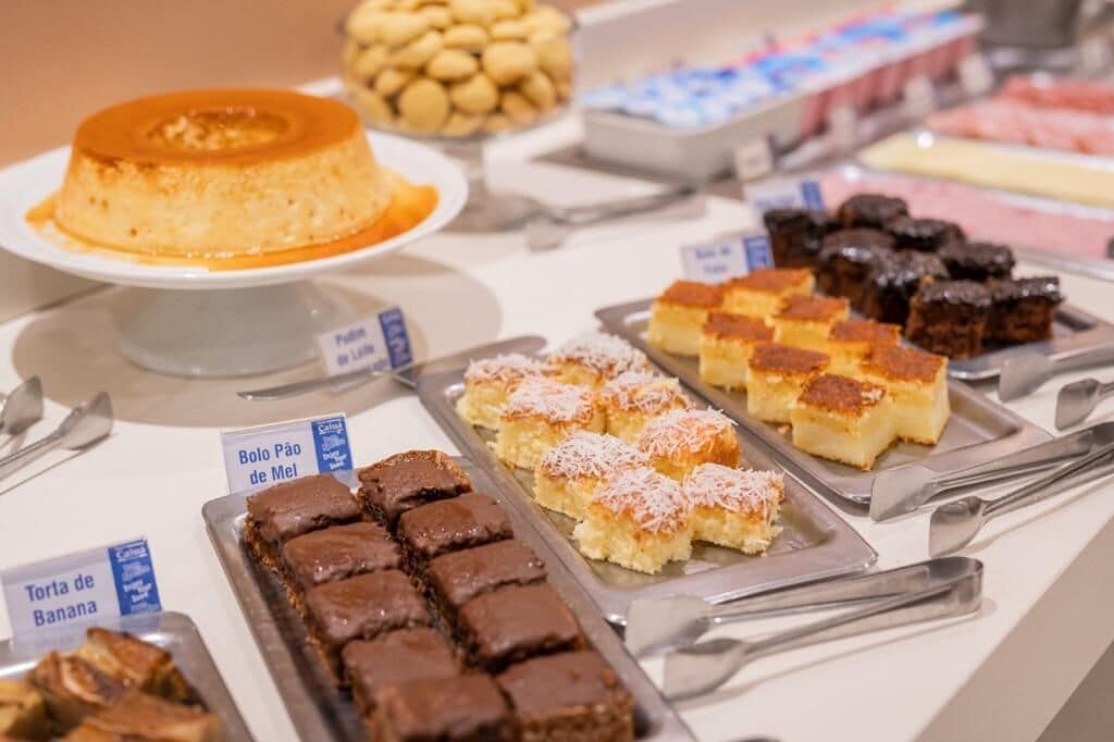 A buffet with various desserts including flan, bolo pão de mel, and torta de banana.