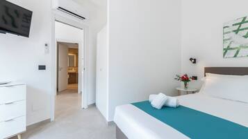 A hotel room with a bed, a desk, a chair, a TV, and a bathroom visible through an open door.