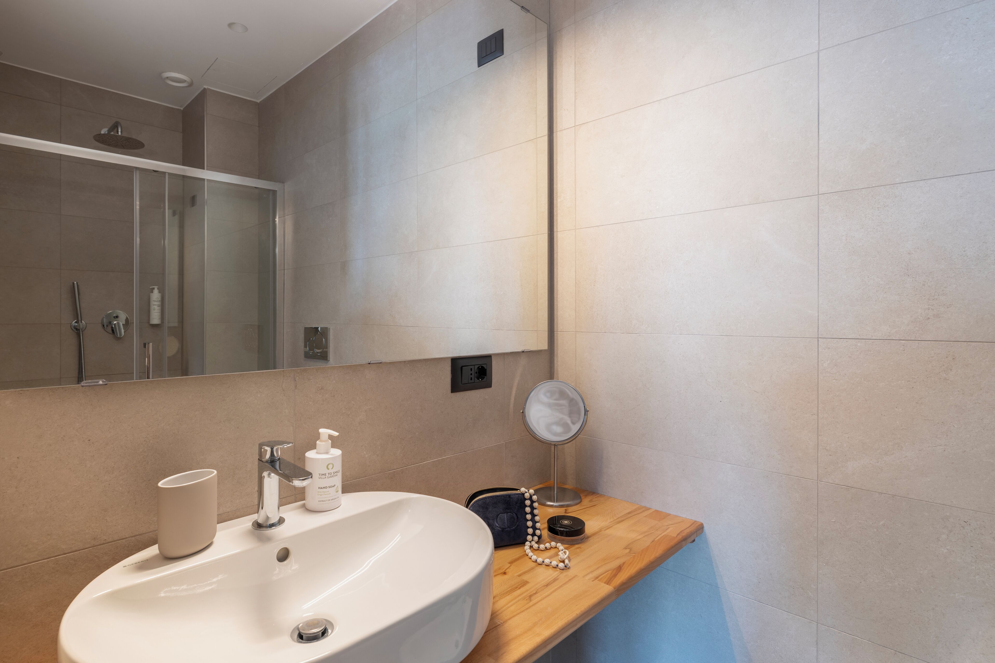Une salle de bain avec un lavabo blanc, un miroir, un plan de toilette en bois et un espace douche.