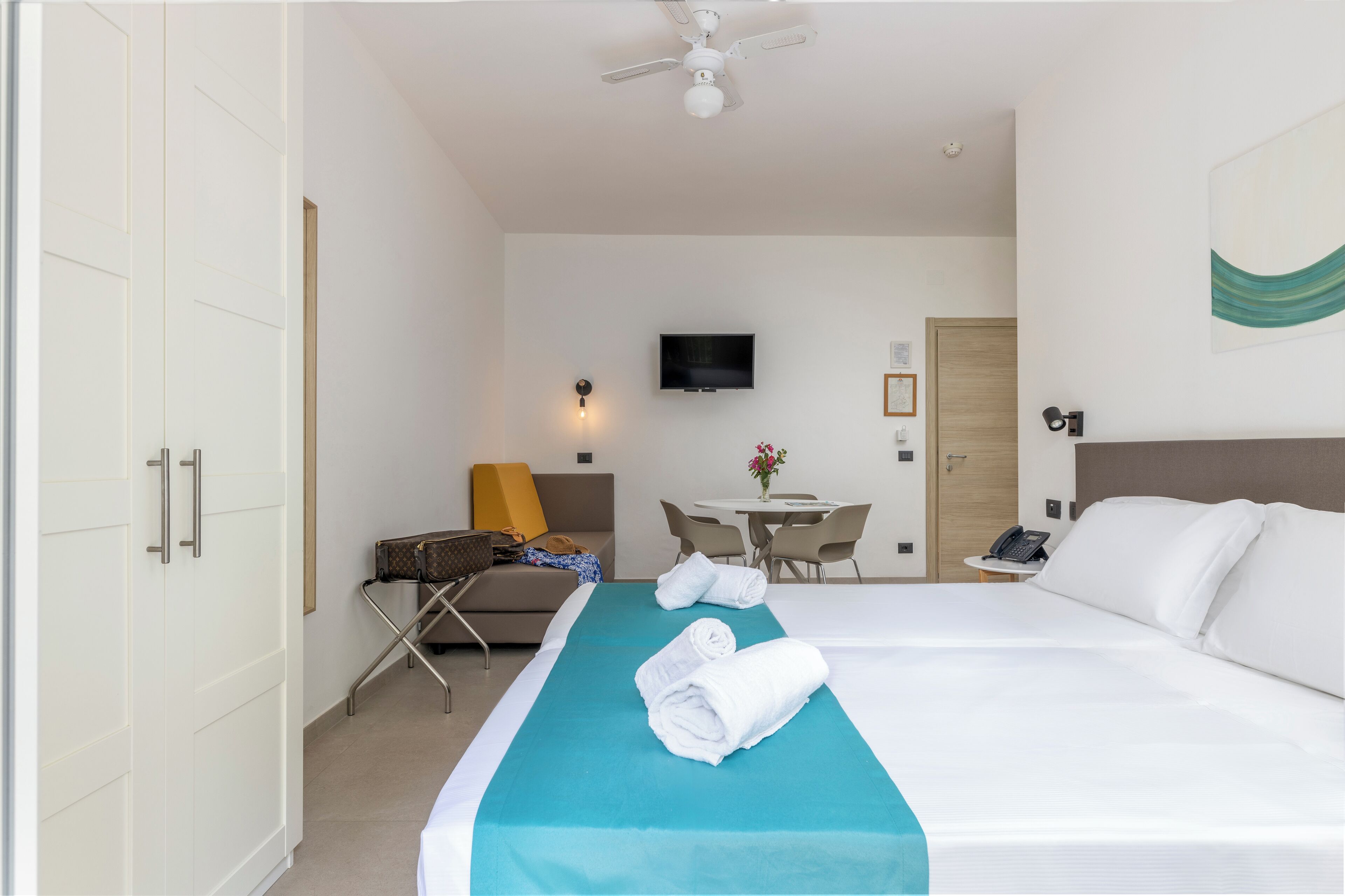A hotel room with a bed, a desk with a chair, a TV, and a telephone.