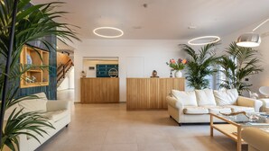 A modern reception area with a wooden reception desk, white sofas, and potted plants. - Residence Villa Giardini (Giardini Naxos)
