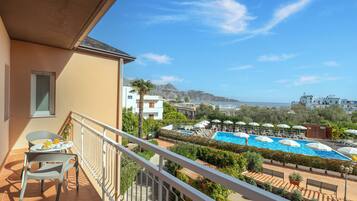 Un balcón con vistas a una piscina, mobiliario exterior y el paisaje de montañas al fondo.