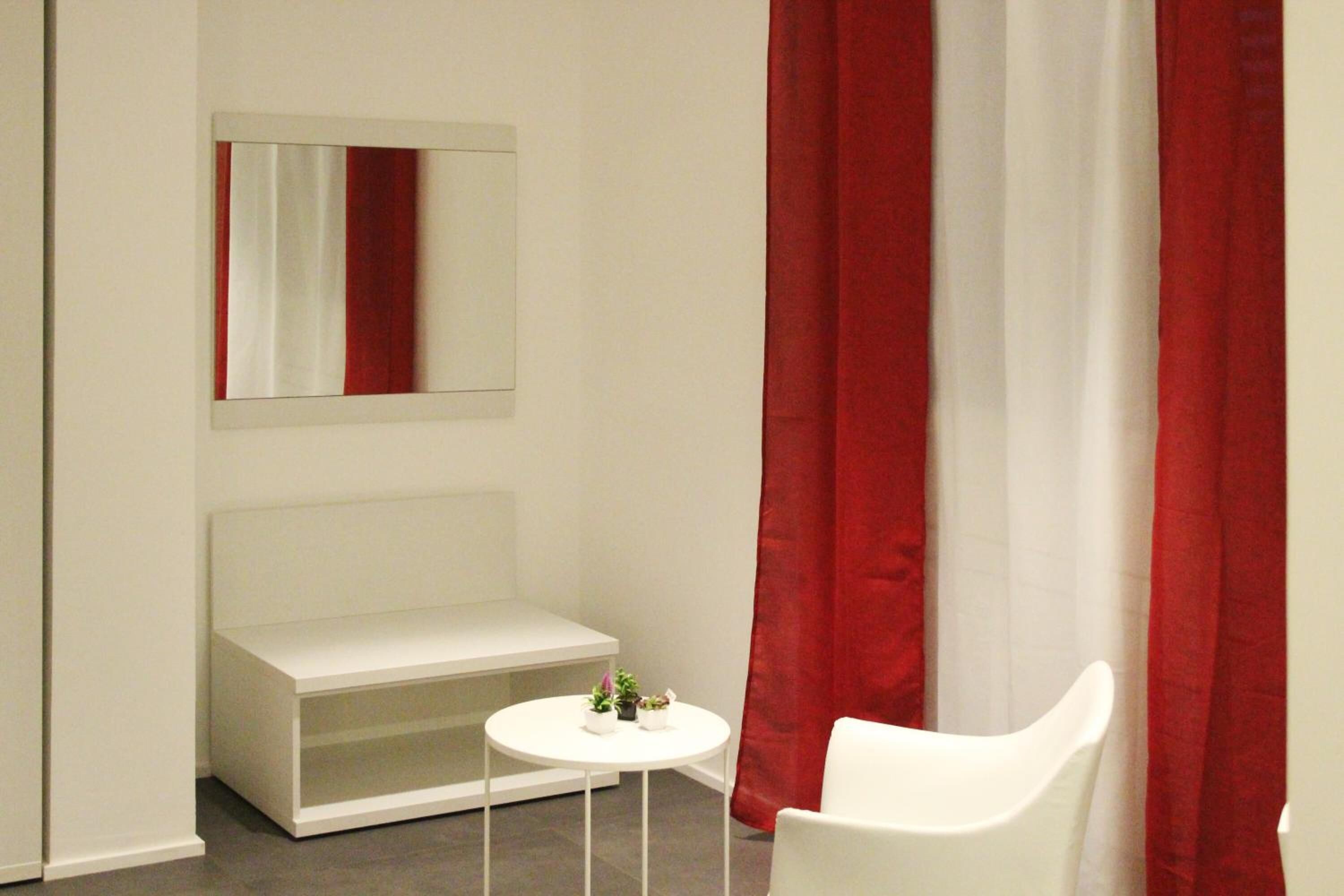 Une chambre moderne avec un banc blanc, une petite table ronde agrémentée d’une plante et des rideaux rouges.