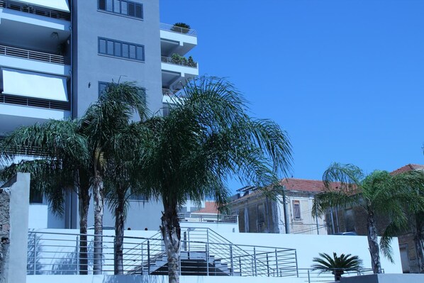 Un edificio moderno con varios balcones, palmeras y un cielo azul despejado.
