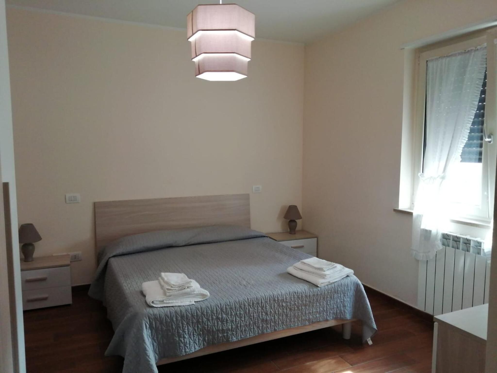 Un dormitorio con cama, mesitas de noche, lámpara y ventana con cortinas.