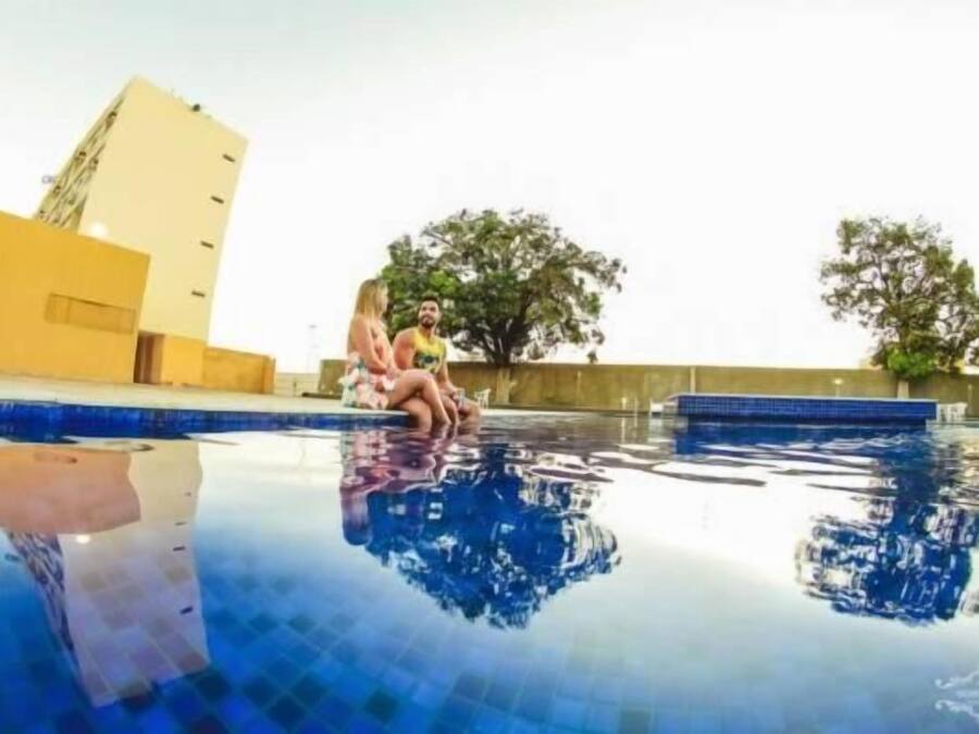 Ein Schwimmbecken mit klarem Wasser, umgeben von einer niedrigen Mauer und einem Gebäude im Hintergrund.