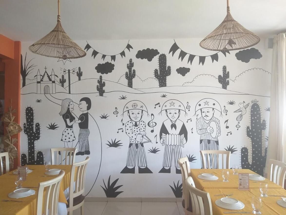 Zona pranzo con un murale raffigurante musicisti e cactus sulla parete, sedie in legno e tovaglia gialla.