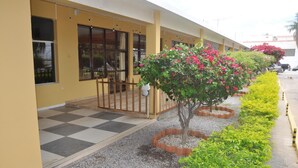 A hotel with a yellow facade, a checkered entrance, and a row of small trees with pink flowers. - Hotel do Grande Rio (Petrolina)
