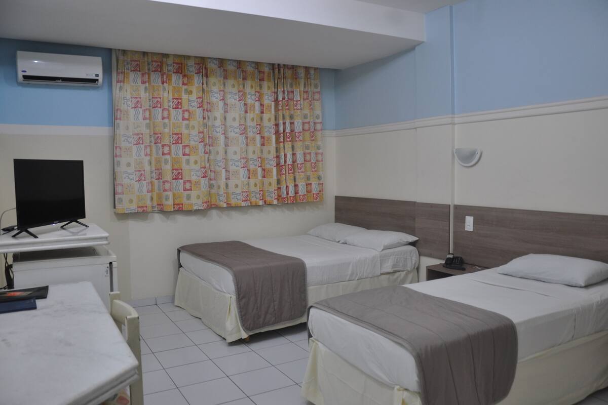 A hotel room with two beds, a desk, a TV, and a patterned curtain.