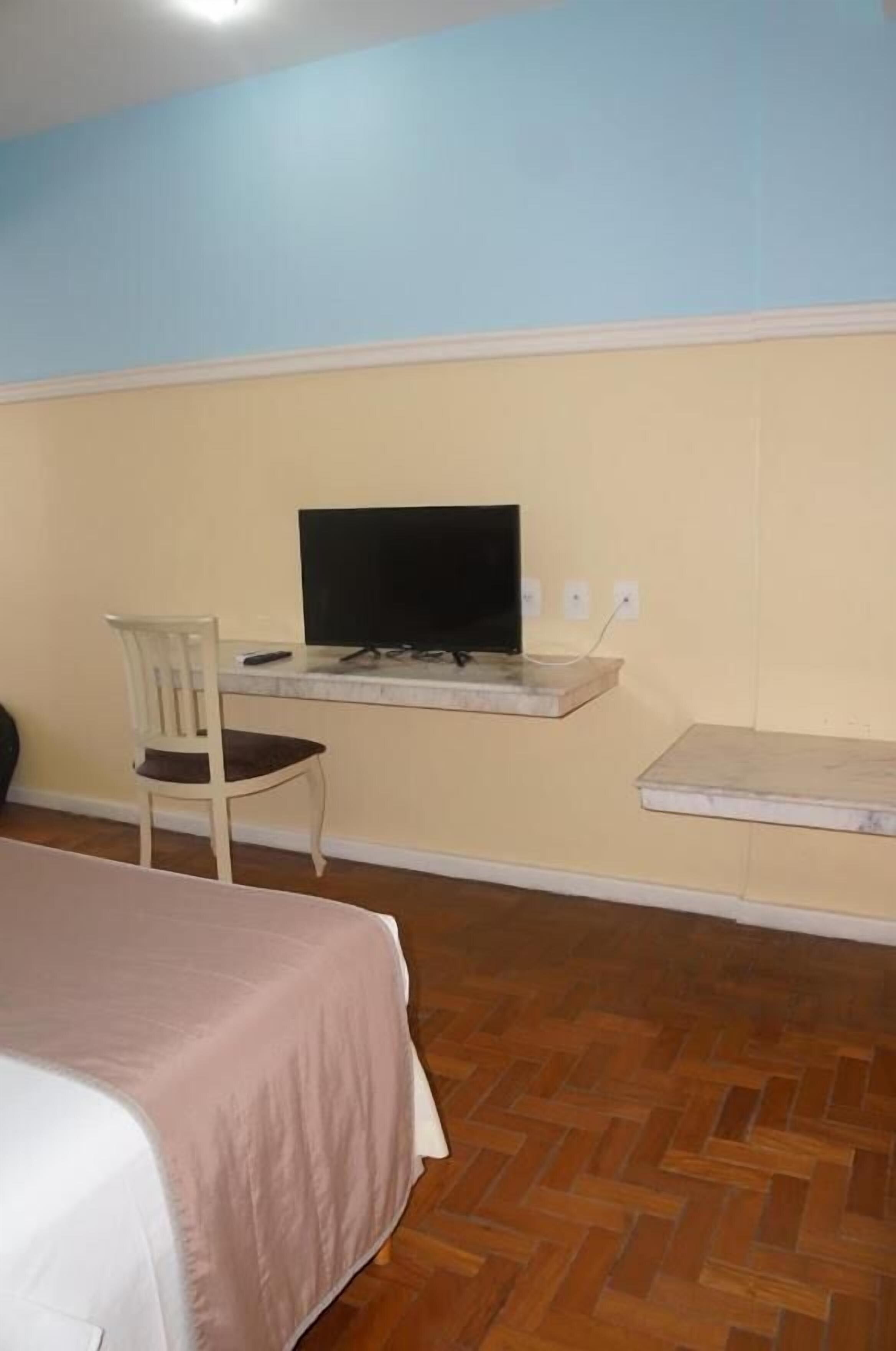 Una habitación con una cama, un escritorio con computadora y una silla.