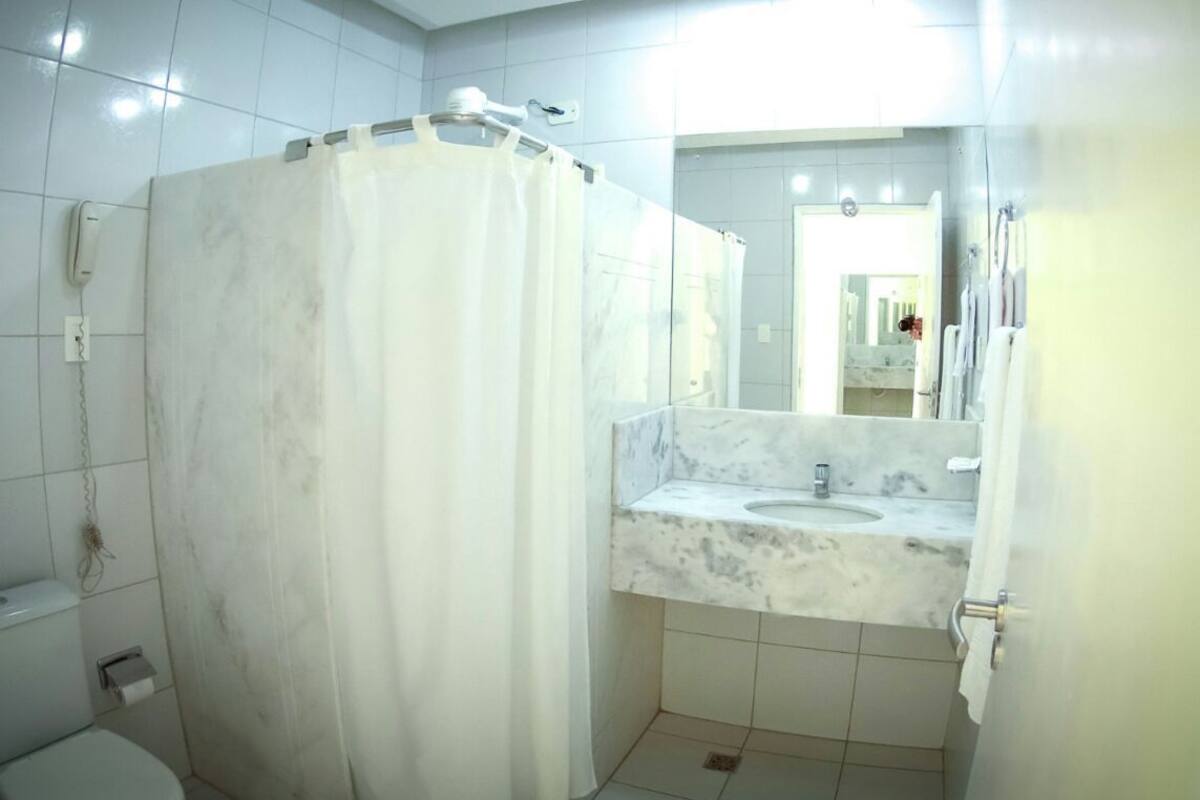 A bathroom with a toilet, a shower curtain, a sink with a marble countertop, and a mirror.