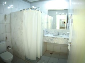 A bathroom with a toilet, a shower curtain, a sink with a marble countertop, and a mirror.
