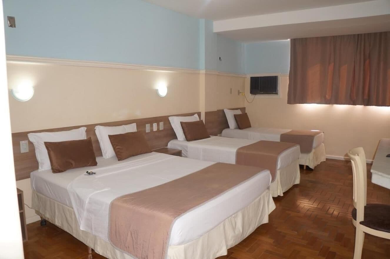 A hotel room with two single beds, a small table, and a chair.