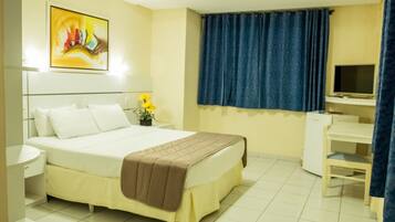 A hotel room with a bed, bedside table, TV, desk, and curtains.
