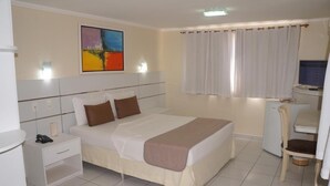 A hotel room with a bed, bedside table, chair, desk, and a painting on the wall. - Hotel do Grande Rio (Petrolina)