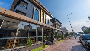 Un hôtel moderne avec une façade en verre, des espaces de détente en plein air et un ciel dégagé.