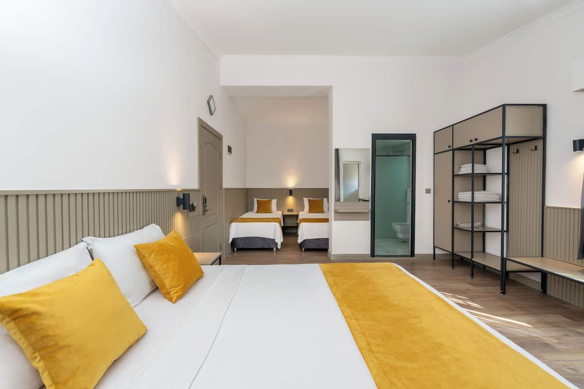 A hotel room with a large bed, two smaller beds, a wardrobe, and a mirror.
