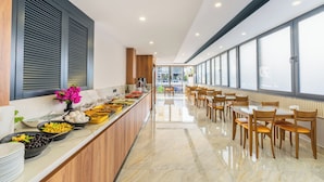 Un espace repas moderne avec un long comptoir, une variété de plats et une rangée de tables et de chaises en bois.