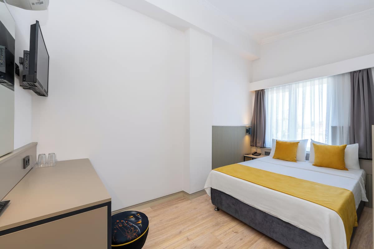 A hotel room with a bed, bedside table, lamp, and a desk with a computer.