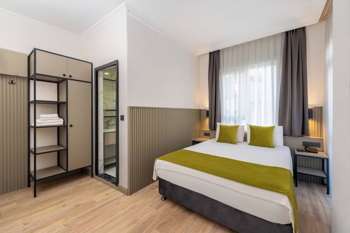 A modern hotel room with a large bed, a wardrobe, a bedside table, and a nightstand.