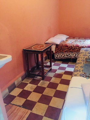 A small room with a checkered floor, a wooden table, a bed with patterned bedding, and a white chair. - Hotel Medina (Marrakech)