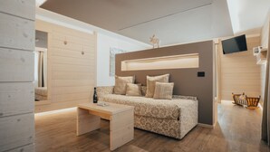 A modern bedroom with a wooden floor, a bed with patterned bedding, a bedside table with a bottle, and a TV mounted on the wall. - Hotel Bezzi (Ponte di Legno)