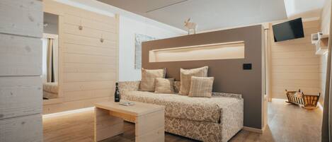 A modern bedroom with a wooden floor, a bed with patterned bedding, a bedside table with a bottle, and a TV mounted on the wall.