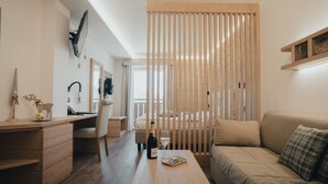 A modern, minimalist living room with a wooden coffee table, a sofa, a desk with a chair, and a large window. - Hotel Bezzi (Ponte di Legno)