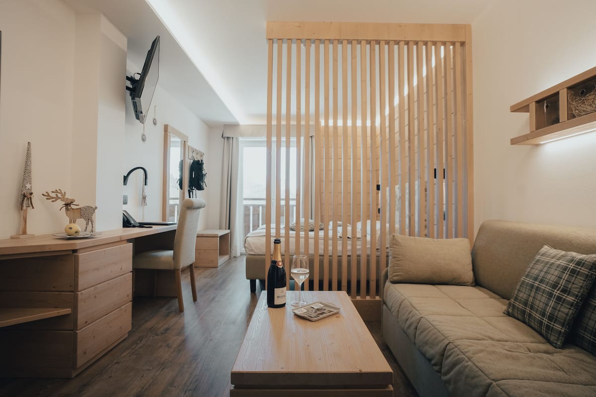 A modern, minimalist living room with a wooden coffee table, a sofa, a desk with a chair, and a large window.