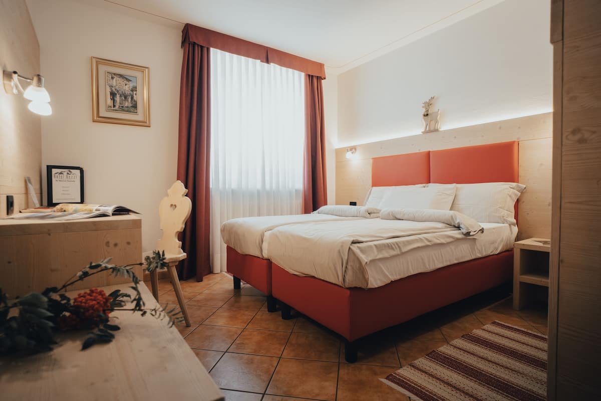 A bedroom with a bed, a dresser, a desk, and a window with curtains.