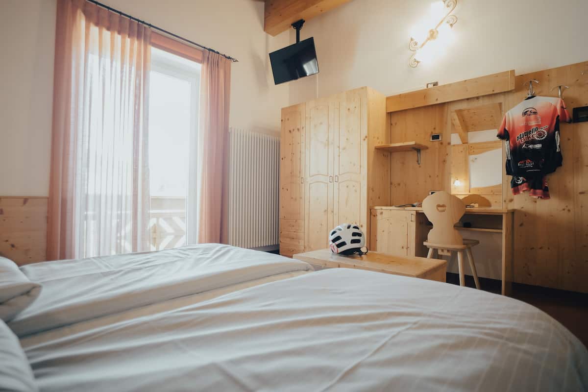 A bedroom with two beds, a wooden wardrobe, a desk, a helmet, and a wall-mounted TV.