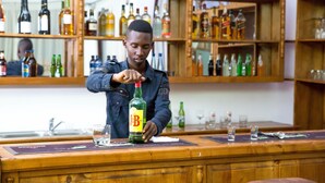 A bar with a bartender preparing a drink. The bar has wooden shelves with various bottles and glasses. - Mountain's View Hotel (Bujumbura)