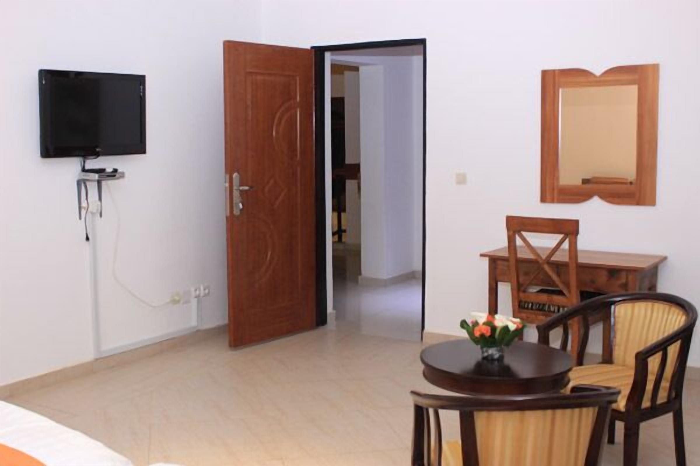 Habitación de hotel con cama, televisor montado en la pared, puerta de madera, mesa de comedor con sillas y un espejo en la pared.